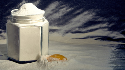 Flour in a jar with a broken egg on a dark background.