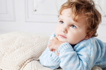 Portrait of happy adorable baby boy on the bed in his room. Thoughtful look up. Copy space