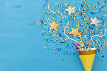 Party colorful confetti and clown hat over blue wooden background . Top view, flat lay.