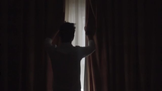 Man Open Big Window Curtains.Man In Dark Room Opens Curtains Slow Motion.Man Unveil Curtains And Admire Garden View From Window In Slow Motion.Man Looking At Window Slow Motion.Guy Stay Against Window