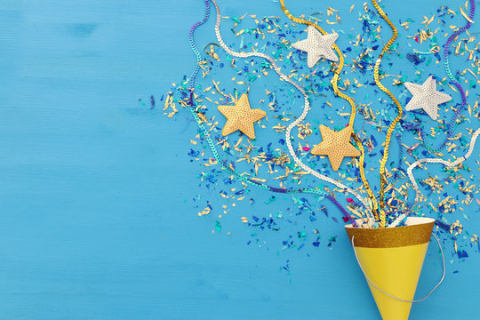 Party colorful confetti and clown hat over blue wooden background . Top view, flat lay.