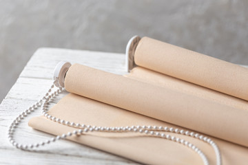 The beige roller blinds is on a wooden surface. Beige blinds lie on an old wooden white table.