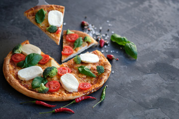 Sliced pizza with Mozzarella cheese, tomatoes, broccoli, Spices and fresh basil. Italian pizza. Pizza on black stone background