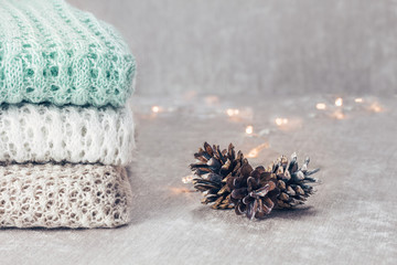 Stylish knitted pastel colored sweaters in different knitting patterns folded in stack with pine...