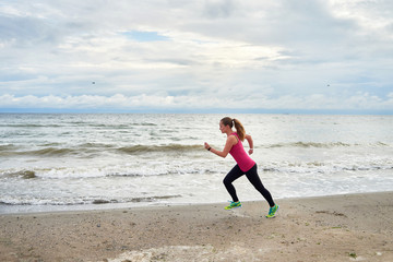 Athletic woman running on sea beach, copy space. Female runner working out at summer morning, full length body portrait, side view. Healthy lifestyle concept