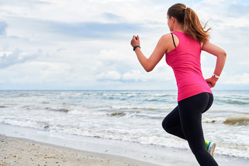 Athletic woman running on sea beach, copy space. Female runner working out at summer morning, back view. Healthy lifestyle concept