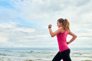 Athletic woman running on sea beach, copy space. Female runner working out at summer morning, side view. Healthy lifestyle concept