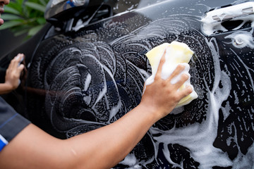 gesture of hand wipe a black car's body with soap and foam