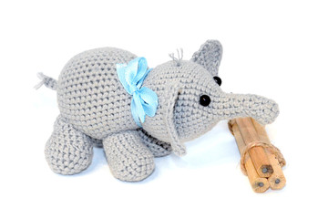 Isolated crocheted gray elephant with a blue bow on the neck stands next to a bunch of wooden pencils on a white background