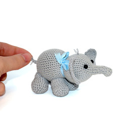 Isolated crocheted gray elephant with a blue bow on the neck on a white background. Female hand holds the elephant by the tail