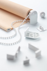 The beige roller blinds is on a white surface. Beige blinds and accessories lie on an white table.