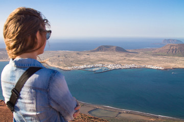 A girl stands turned backs against the background of the Atlantic Ocean and the island of La Graciosa. Mountain. Mirador del Rio. North of Lanzarote. Canary Islands. Spain