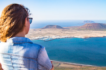 A girl stands turned backs against the background of the Atlantic Ocean and the island of La Graciosa. Mountain. Mirador del Rio. North of Lanzarote. Canary Islands. Spain