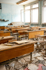 Fototapeta na wymiar The thrown and destroyed school in Pripyat after the Chernobyl accident in Ukraine in 1986. School desks and scattered textbooks in one of the school classes.