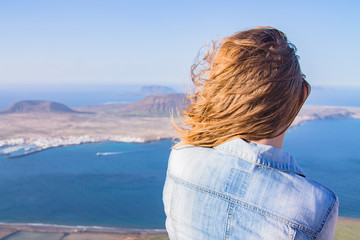 Fototapeta na wymiar A girl stands turned backs against the background of the Atlantic Ocean and the island of La Graciosa. Mountain. Mirador del Rio. North of Lanzarote. Canary Islands. Spain
