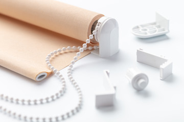 The beige roller blinds is on a white surface. Beige blinds and accessories lie on an white table.