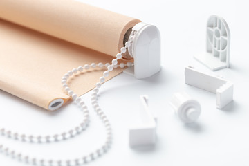 The beige roller blinds is on a white surface. Beige blinds and accessories lie on an white table.