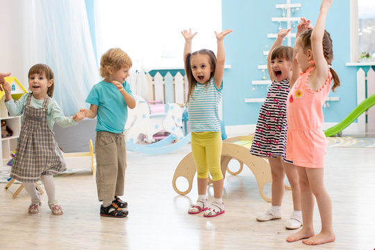 Group of expressive preschool children with raising hands while having fun in entertainment center