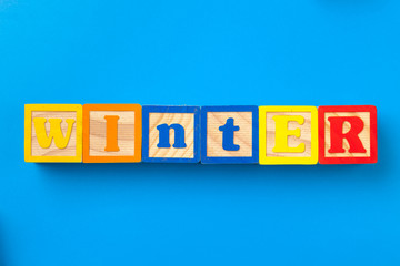 Winter. Wooden colorful alphabet blocks on blue background, flat lay, top view.