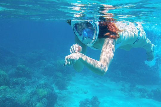 Woman in bikini show time underwater. Snorkeling in tropical sea coral reef. Young girl in full-face snorkeling mask
