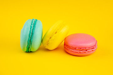 Sweet almond colorful macaron or macaroon dessert cake isolated on trendy yellow pastel background. French sweet cookie. Minimal food bakery concept. Flat lay copy space