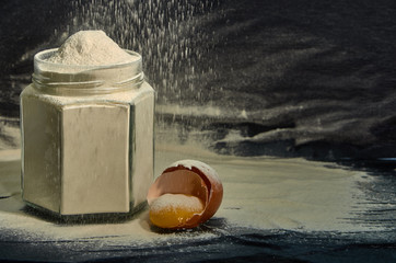 Flour in a jar with a broken egg on a dark background.