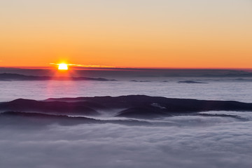 Obraz premium Beautiful sunset over a valley filled by fog with mountains and hills