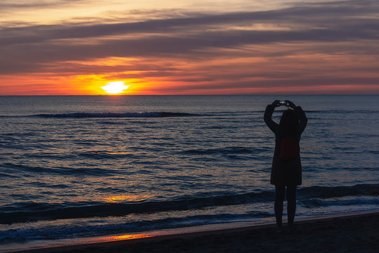Woman taking pictures at sunset with smartphone