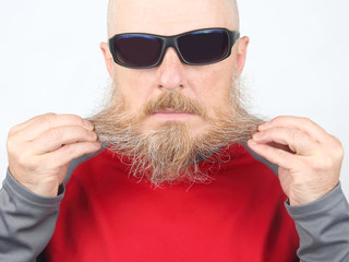 Portrait of a bald, bearded man wearing dark glasses on a light background