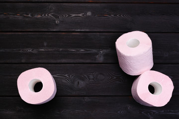 Pastel pink toilet paper rolls on black wooden background