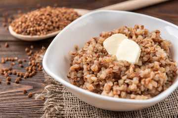 Buckwheat porridge with butter on dark wooden background.