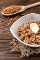 Buckwheat porridge with butter on dark wooden background.