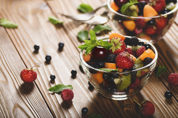 Assorted fruits in glass bowl on kitchen wooden table with fork aside