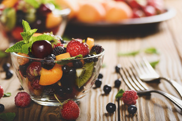 Assorted fruits in glass bowl on kitchen wooden table with fork aside