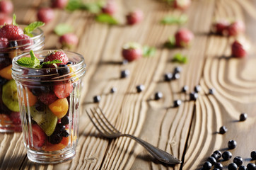 Assorted berries in mason jar on kitchen wooden table with fork aside