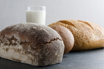 Fresh backed rye bread,bread with sesam seeds, rye bun, glass f milk on dark table in the kitchen.Closeup of different kinds of bread.Rustic moon