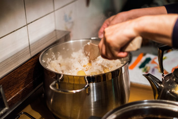 Hand chef using wooden flipper mixing rice with potato in pot