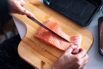 Hand chef using knife slice raw salmon on chopping board