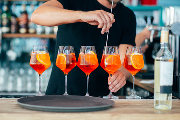 Five colored cocktails prepared by a bartender with pieces of orange and ice cubes
