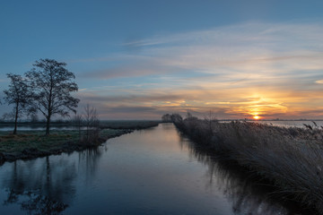 Sunrise above a ditch and a lake dike silhouettes of trees. Reeuwijk The Netherlands Europe.