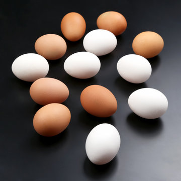 different chicken eggs lie randomly on dark background