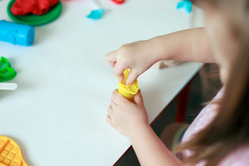 Child playing with colorful clay molding different shapes - closeup on hands, copy space