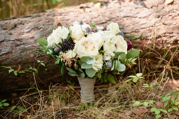 Close up of small bridal bouquet of white peonies, roses and greenery with satin ribbon on wood background outdoors, copy space. Wedding concept