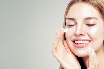 Closeup beauty portrait of laughing woman with healthy skin applying cosmetic cream on her face. Skin care, beauty and facial treatment concept