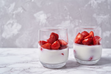 Two glasses of healthy yogurt with fresh sliced strawberry on white marble table background, copy space. Healthy breakfast, food concept