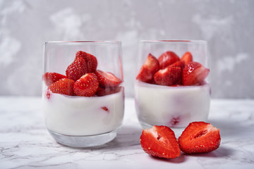 Two glasses of healthy yogurt with fresh sliced strawberry on white marble table background, copy space. Healthy breakfast, food concept