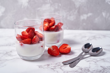 Two glasses of healthy yogurt with fresh sliced strawberry and spoons on white marble table background, copy space. Healthy breakfast, food concept