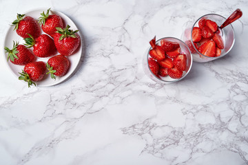 Obraz na płótnie Canvas Two glasses of healthy yogurt with fresh sliced strawberry and spoons on white marble table background, copy space. Healthy breakfast. Top view, flat lay