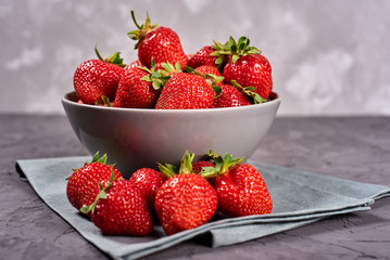 Red ripe strawberry in ceramic bowl on linen table napkin on gray concrete background, copy space. Healthy food concept, still life