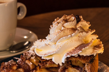 Dutch apple pie with a whipped cream and a chocolate coffee bean on it on a table with a coffee cup...